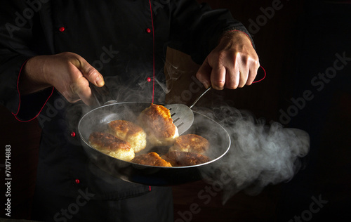 Fototapeta Naklejka Na Ścianę i Meble -  A baker prepares pancakes in a frying pan. The concept of preparing a national dish or pancakes in the kitchen. Dark space for advertising.