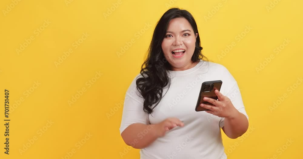 A chubby Asian woman wearing a white t-shirt was excited and happy when she saw a message on her phone on a yellow background. A chubby Asian woman wearing a white t-shirt was excited and happy when she saw a message on her phone on a yellow background.