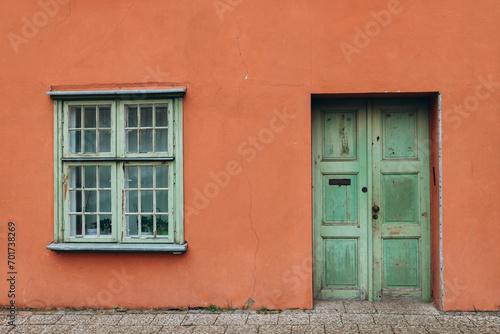 A vintage red house with old green door and window. Ancient wooden door in old building wall.