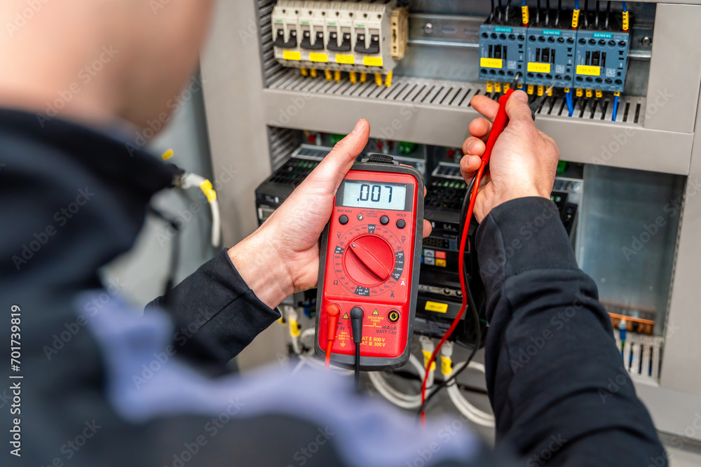 Worker measuring and repairing an electrical system panel - obrazy, fototapety, plakaty 