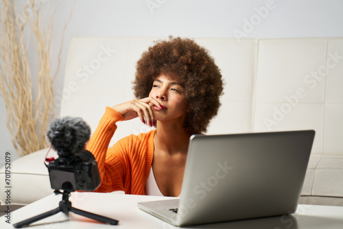 young latina woman with afro hair thinking about editing a video for social networking uses laptop