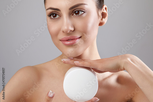 Skin care. Beauty Concept. Young woman holding cosmetic moisturizing cream. Soft skin and naked shoulders, model with light nude make-up, portrait of girl face with clean healthy skin. Dermatolog