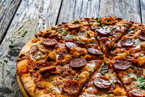 Circle pizza chorizo with chicken nuggets and mozzarella, on wooden table 