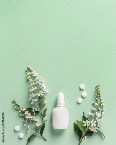 Seasonal allergy concept, spring blooming branches tree and mock up nasal spray white bottle, pills on green background, top view, flat lay. Healthy lifestyle, treatment seasonal allergies photo