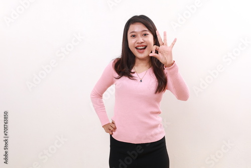 Satisfied young asian girl standing while showing okay hand gesture. Isolated on white