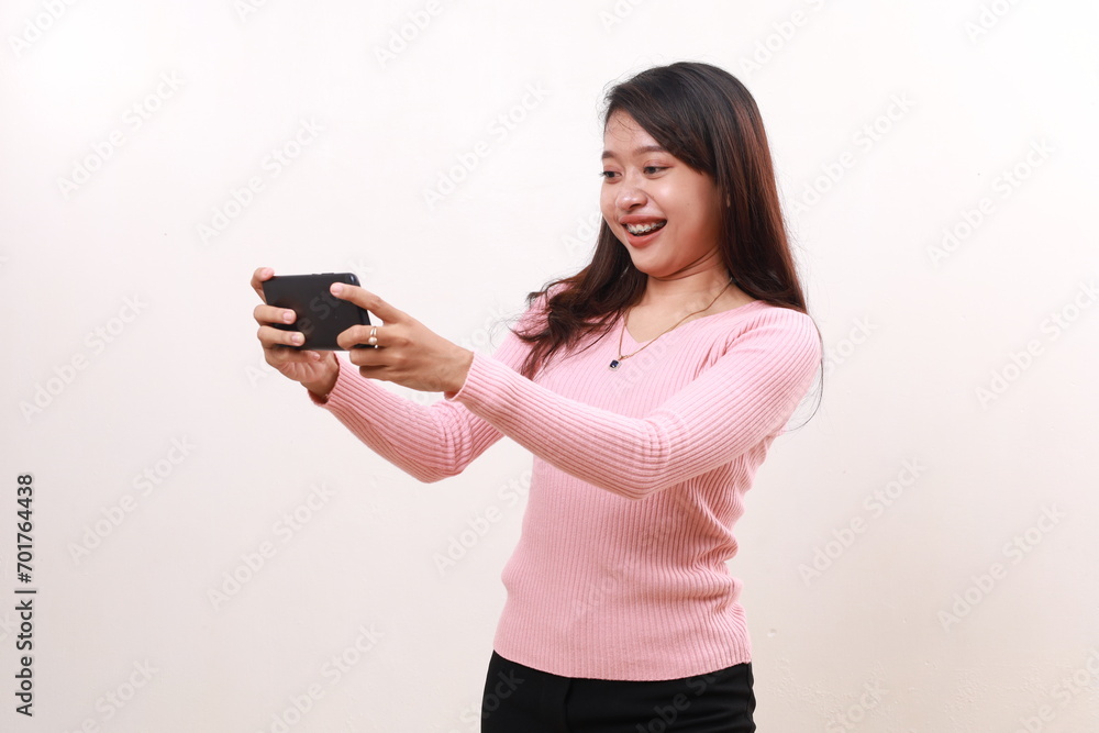 Happy young asian girl standing while playing game on her phone. Isolated on white background Happy young asian girl standing while playing game on her phone. Isolated on white background