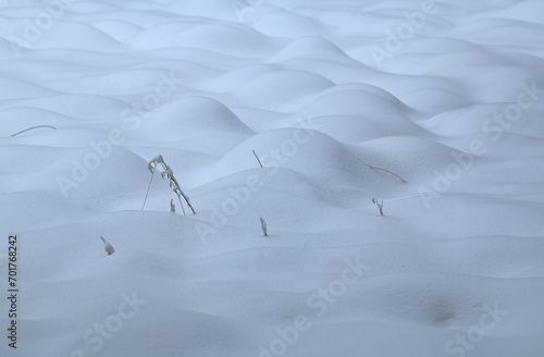Eine Graswiese ist bedeckt von hohem Schnee und nur vereinzelt ragen Grashalme aus den Schneehügeln, Es ist eine kleine Berg und Tallandschaft aus Schnee. photo