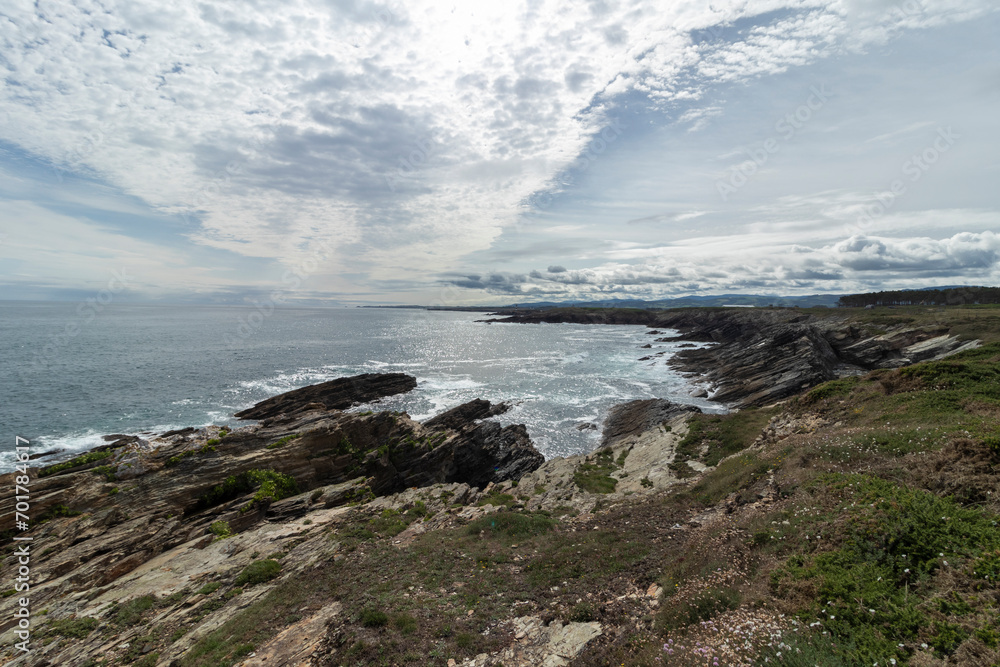 rugged coastline with erosion, sparse vegetation, glistening ocean, and a partly cloudy sky. Serene and dynamic landscape