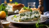  a slice of spinach and cheese quiche on a white plate with a fork on a wooden table next to a glass of water.