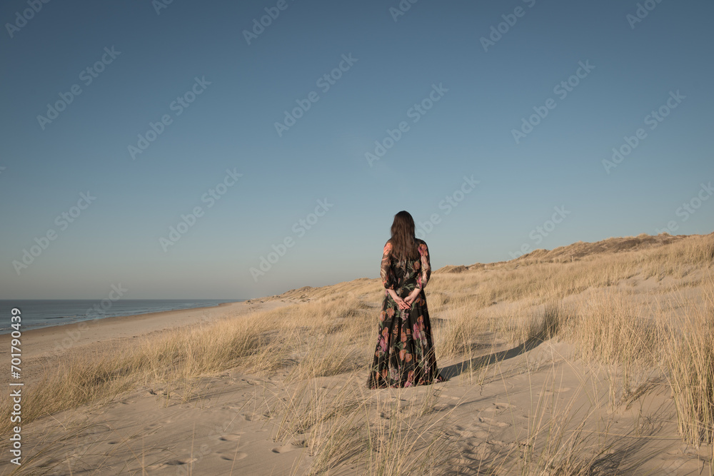 © Milou Dirks - woman in long dress standing alone in the dunes near the beach