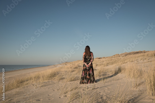 woman in long dress standing alone in the dunes near the beach photo