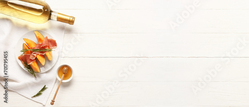 Fototapeta Naklejka Na Ścianę i Meble -  Plate with delicious melon, prosciutto, rosemary, honey and bottle of wine on white wooden background with space for text