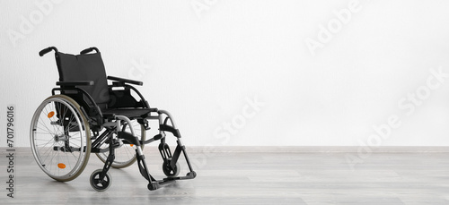 Modern empty wheelchair near white wall. Banner for design