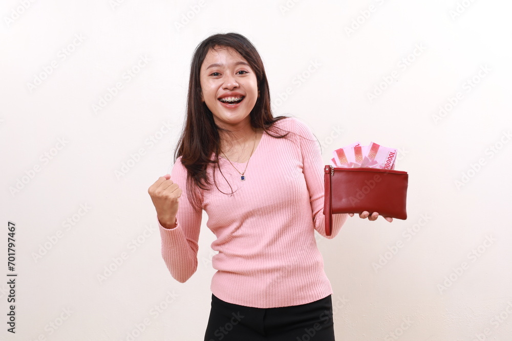 Excited young asian girl celebrating success with fist hand while holding Indonesia banknotes on her wallet. Isolated on white Excited young asian girl celebrating success with fist hand while holding Indonesia banknotes on her wallet. Isolated on white