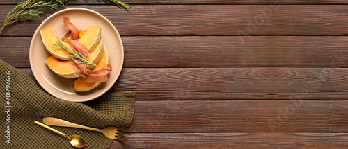 Fototapeta Naklejka Na Ścianę i Meble -  Plate with tasty melon, prosciutto and rosemary on brown wooden background with space for text