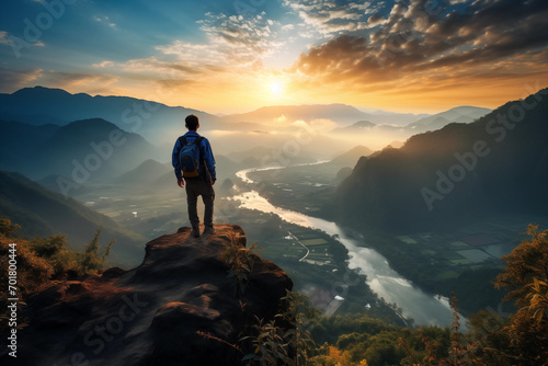A man stands on top of a cliff overlooking a valley at sunset © xtremeisz