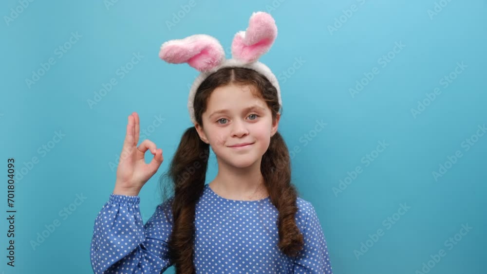 Portrait of beautiful smiling preteen girl kid wearing pink bunny ears and casual dress, happy looking at camera, showing okay sign with fingers, posing isolated over blue studio background wall Stock ビデオ | Adobe Stock