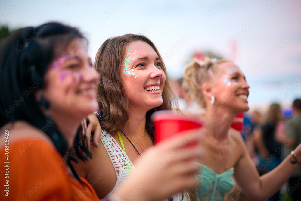 Three Female Friends Wearing Glitter Having Fun At Summer Music Festival Holding Drinks