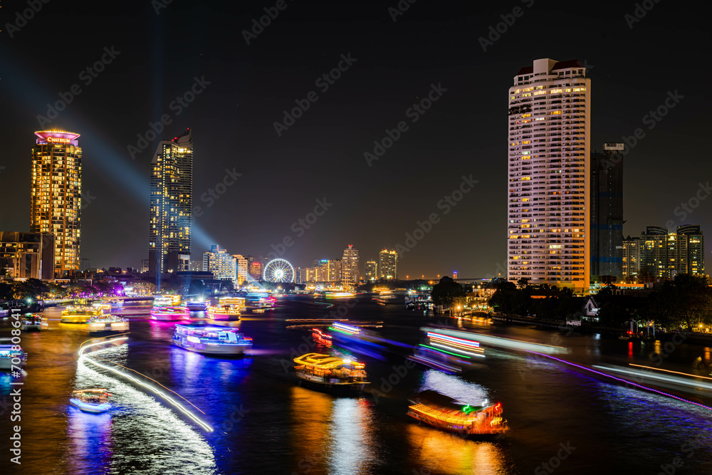 Naklejka premium Night light landscape along the Chao Praya River, having some boats come to celebrate the New Year eve on the Asiatique landmark side in Bangkok city, Thailand.