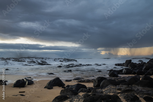 Long exposure shot of the waves crashing on the rocky shore and the rain clouds approaching the coast of Benares beach in a morning on the south coast of Mauritius island 