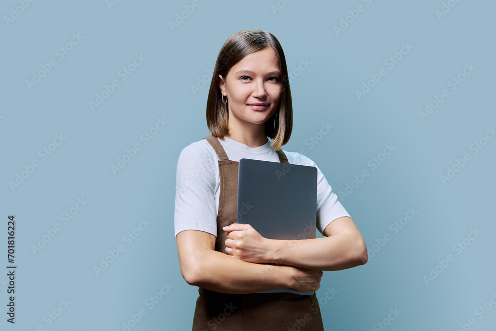 Portrait of young woman in apron holding laptop on blue background Portrait of young woman in apron holding laptop on blue background