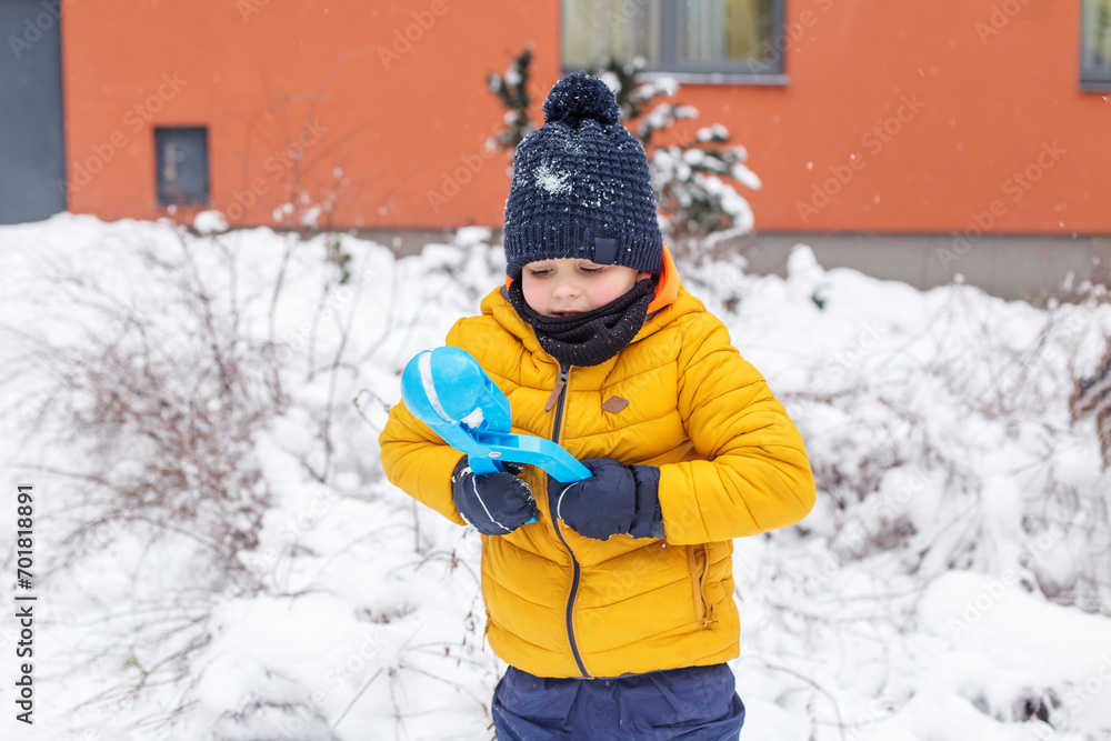 Winter games outdoors. Small boy have fun making snowballs with toy plastic maker.