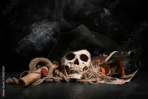 Human skull with toy model of cannon, pirate hat, world map and scroll on black background