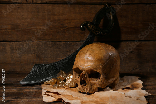 Human skull with sword, old manuscripts and golden nuggets on brown wooden background