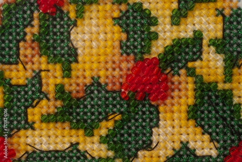 A close-up shot of a cross stitch made with yellow and green threads, red and green beads.