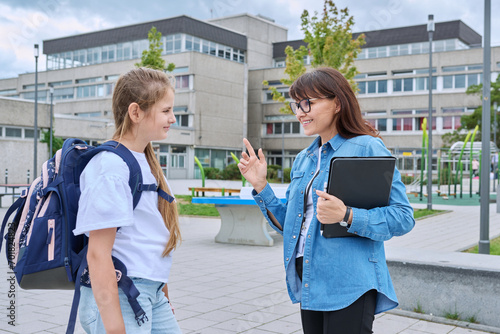 Talking teacher and schoolgirl child outdoor, school building background photo