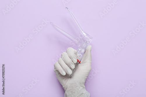 Hand in medical glove and with gynecological speculum on lilac background photo