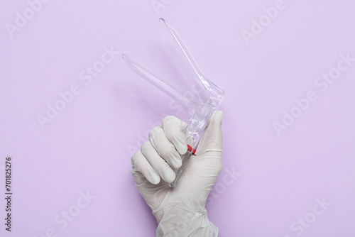 Hand in medical glove and with gynecological speculum on lilac background