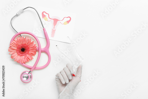 Hand in medical glove, with gynecological speculum, drawing of female uterus and stethoscope on white background photo