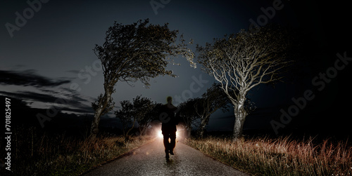 Männliche Person auf einer Waldstrasse im Scheinwerferlicht als Schemenhafte Silhoutte