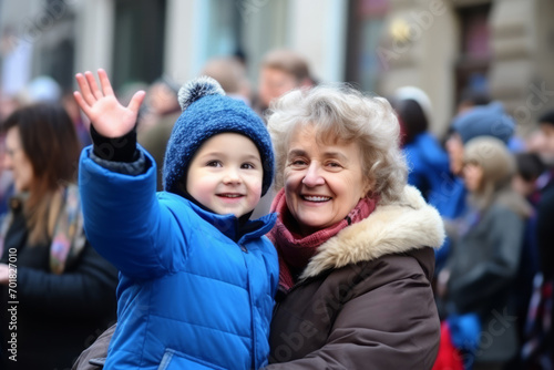 Smiling grandmother holds her grandson and enjoys the Three Kings Parade on the street. Family unity  spending time together  family holidays