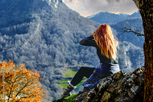 Red-haired girl in black with her back to the viewer on the background of vividly painted mountains, gorge, valley. Travel, tourism.