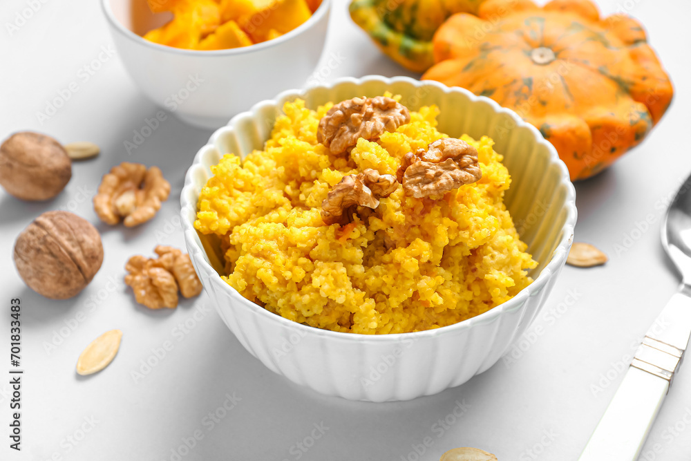 Bowl of tasty millet porridge with pumpkin and nuts on grey background