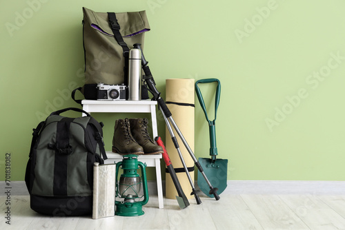 Set of camping equipment with backpack, oil lantern and outdoor gear near green wall