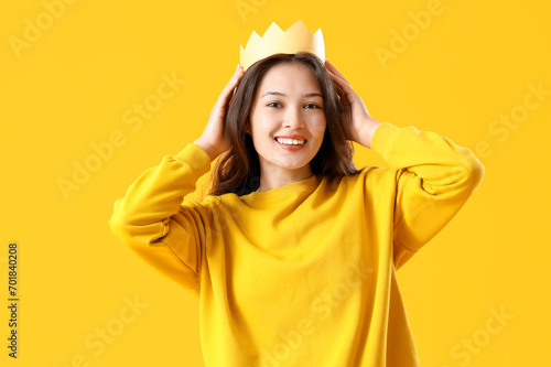 Young Asian woman in paper crown on yellow background © Pixel-Shot