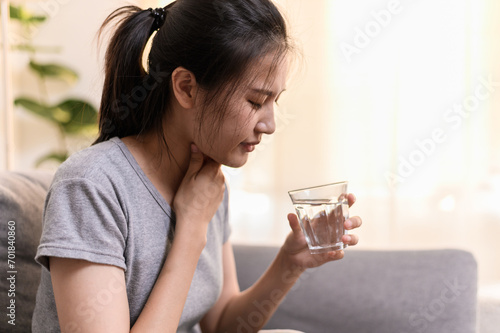 Young Asian woman have a sore throat or have a sick fever taking a medicine and drinking water while sitting on sofa at home. photo