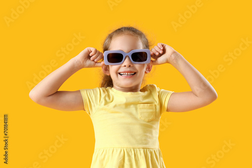 Cute little girl in sunglasses on yellow background