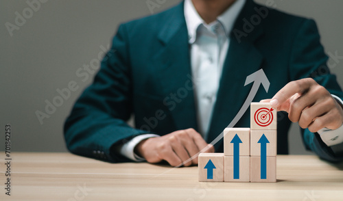 Businessman stacking wooden blocks with icon business goals and up arrow for business objective. Strategic planning for business growth and target customer group.