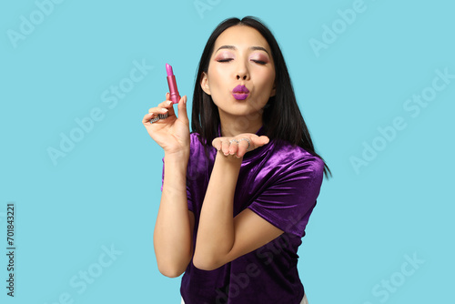 Beautiful Asian woman with lipstick blowing kiss on blue background photo