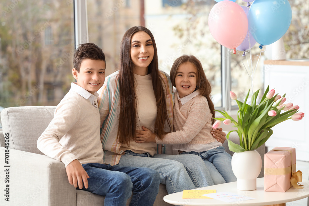 Young woman with her little children sitting on sofa at home. Mother's Day celebration Young woman with her little children sitting on sofa at home. Mother's Day celebration