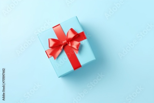 Gift box with red bow ribbon on light blue table top view. Greeting card for Christmas or New Year 3D 
