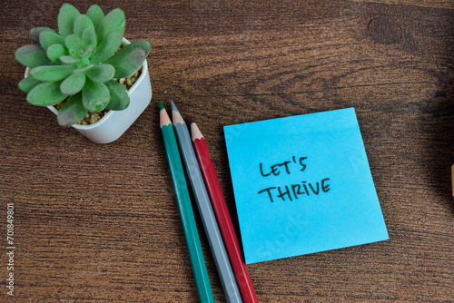 Concept of Let's Thrive write on sticky notes isolated on Wooden Table.