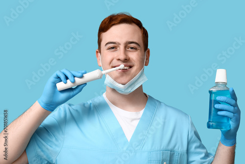 Male dentist with electric toothbrush and bottle of mouth rinse on blue background. World Dentist Day photo