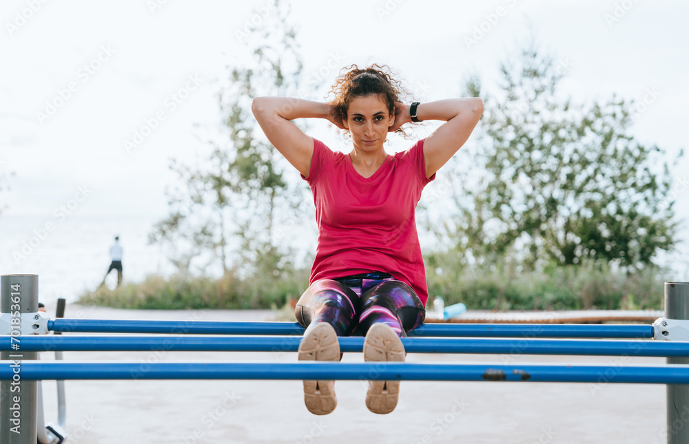 Determined woman doing sit-ups on outdoor fitness equipment with natural scenery in the background