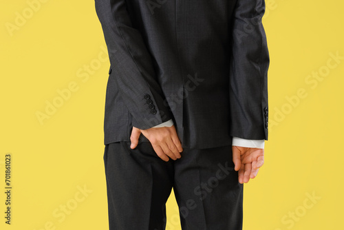 Young businessman with hemorrhoids on yellow background, back view © Pixel-Shot