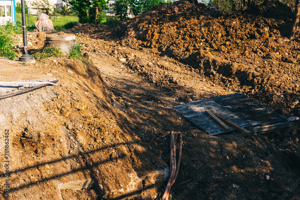 Fototapeta premium an open pit with a loader for laying pipes. a paved road to improve communications in the city. preparation of trenches for construction work